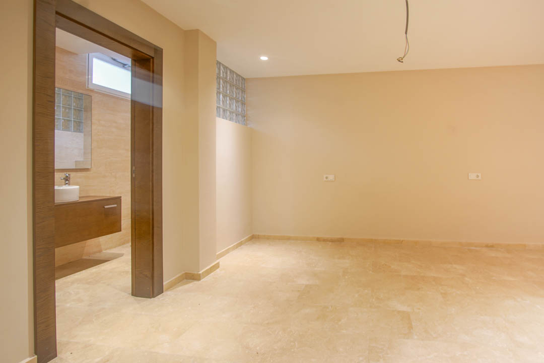 Bedroom featuring natural stone flooring and an en-suite bathroom. Highlights include a floating wooden vanity, glass block windows, and neutral-toned walls.