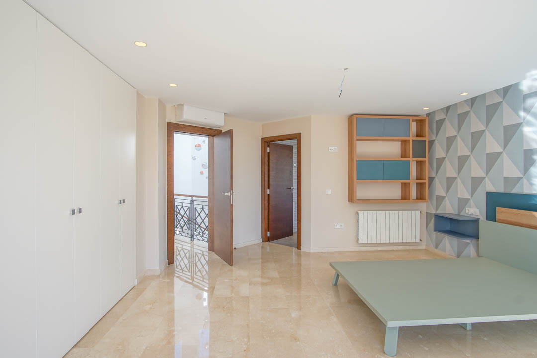 Bedroom featuring polished marble flooring, floor-to-ceiling white wardrobes, and a geometric accent wall. Includes a custom wooden shelf and views toward the landing.