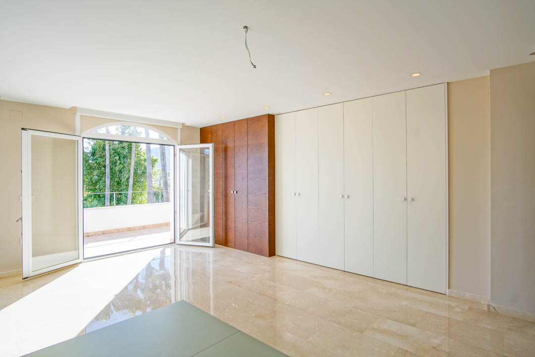 Bright bedroom featuring custom two-tone built-in wardrobes, polished marble floors, and direct access to a private terrace overlooking the palm garden.