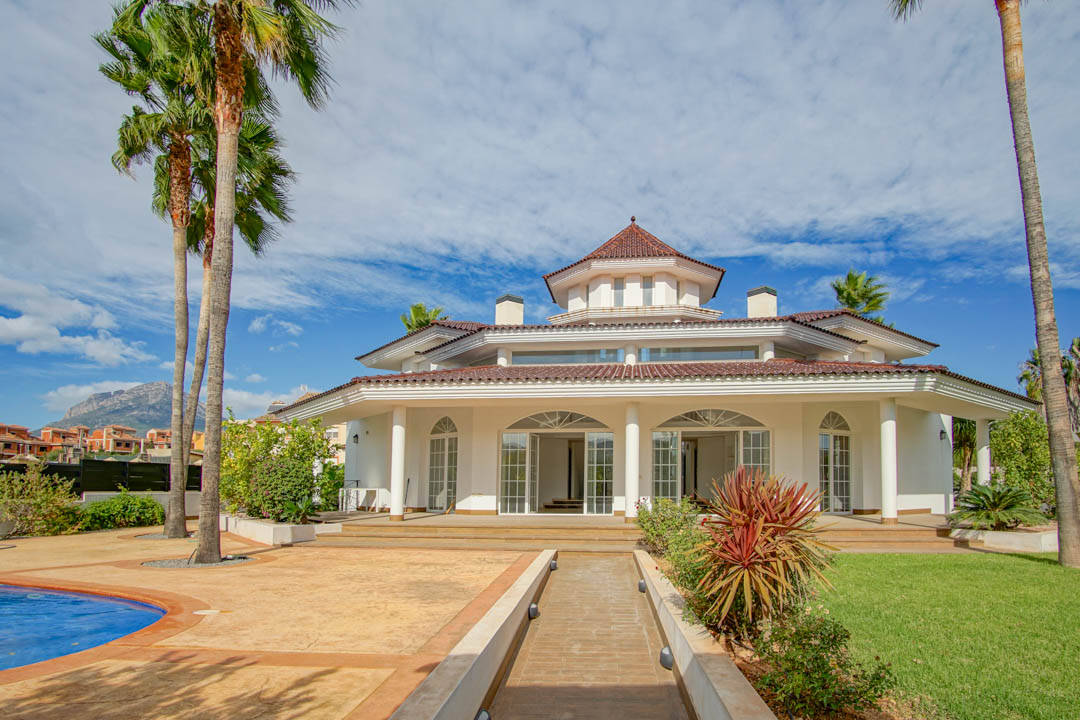 Colonial-style exterior featuring a white facade with columns, a central octagonal tower, and a landscaped garden with mature palms and a pool.