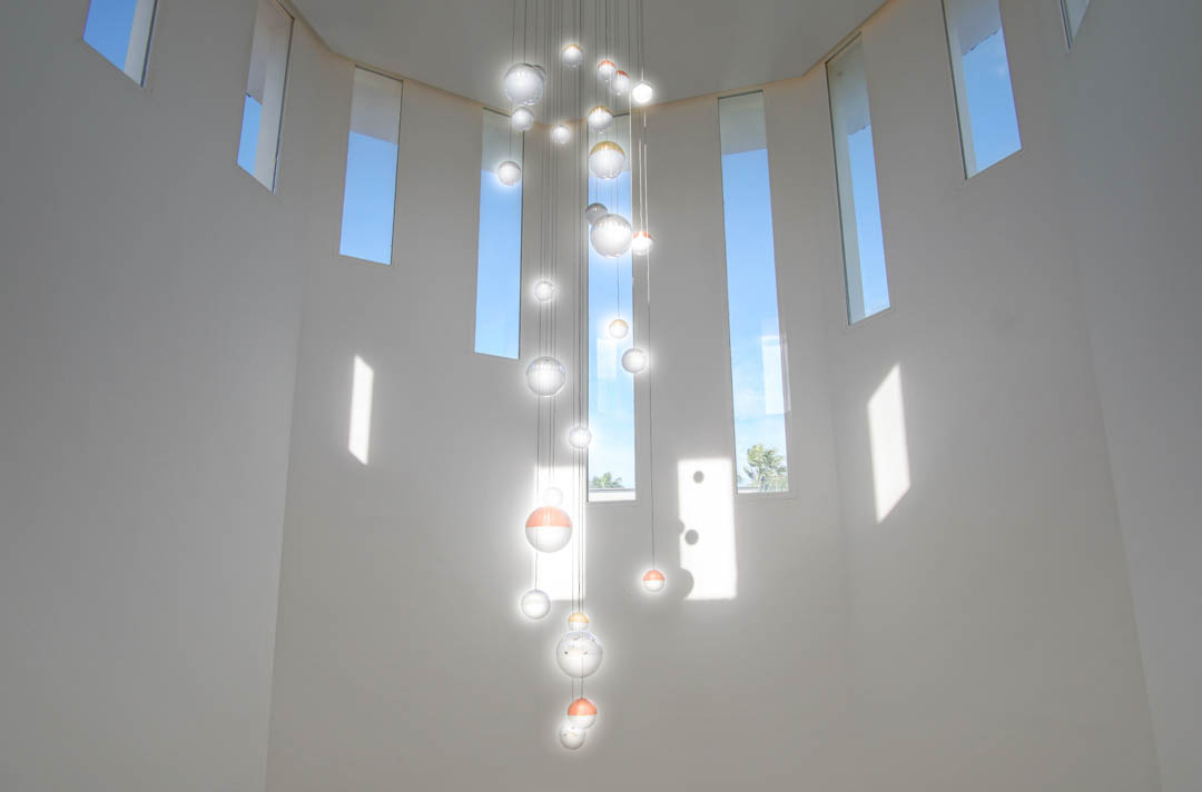 Double-height ceiling featuring a modern multi-sphere glass chandelier and several narrow vertical windows that flood the hall with natural light.