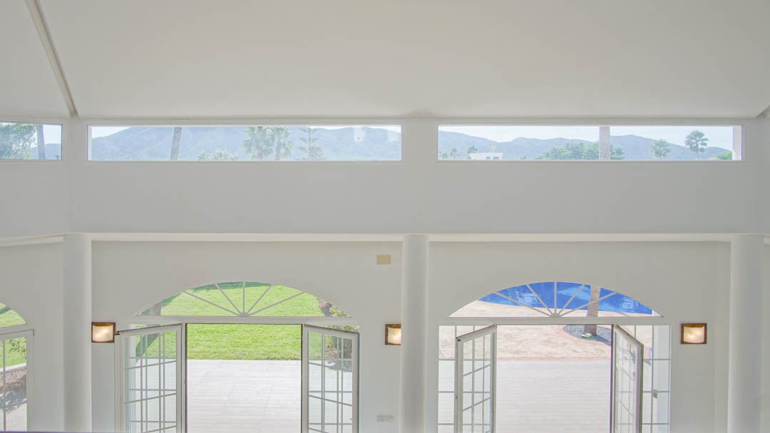 Double-height living space featuring arched doors to the garden and pool, with upper clerestory windows offering views of the mountains and palms.