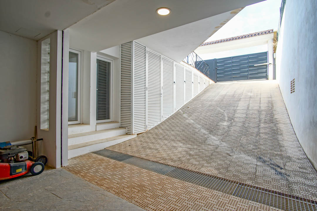 Garage access ramp featuring a non-slip surface, white louvered storage doors, and a secondary entrance with glass doors and white steps.