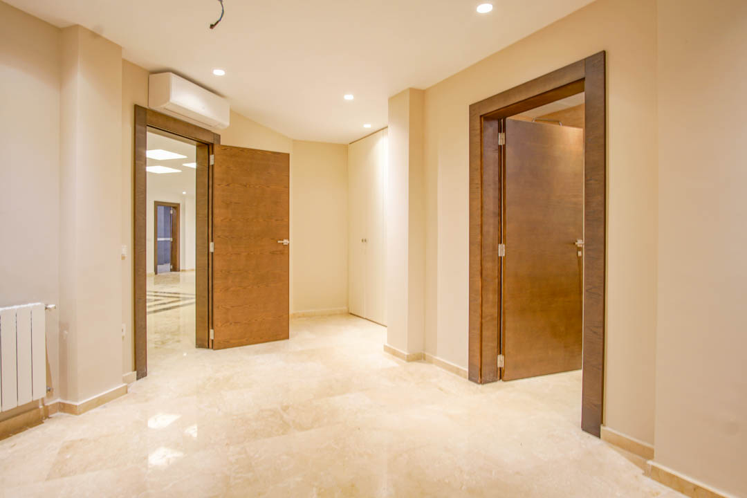 Hallway featuring polished marble flooring, solid wood doors with dark frames, and recessed ceiling lighting. Includes built-in white wardrobes and wall-mounted climate control.