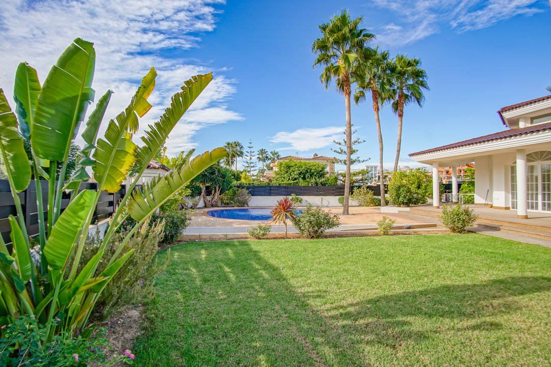 Mature garden featuring a manicured lawn, tall palm trees, and a circular private pool adjacent to a colonial-style porch with white columns.