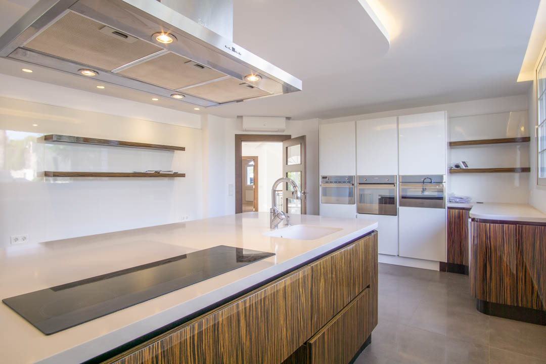 Modern kitchen featuring a large island with induction cooktop, wood-grain cabinetry, and integrated appliances. Highlights include white countertops and stainless steel extractor.