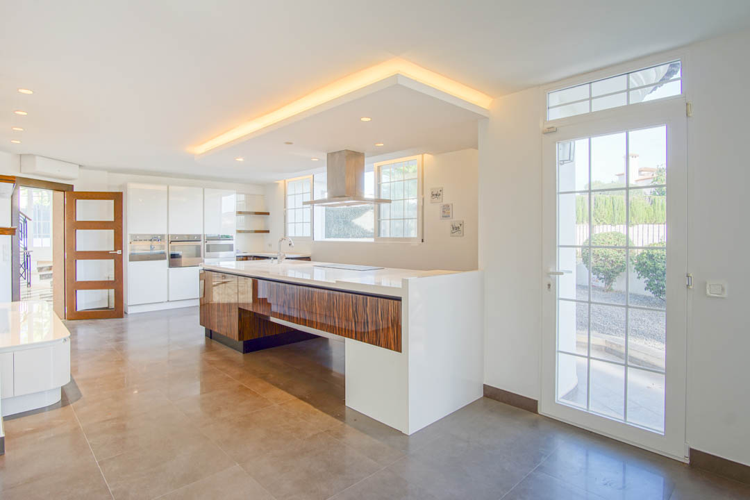 Modern kitchen featuring a large wood-paneled island with white countertops, integrated appliances, and a recessed ceiling with ambient LED lighting.