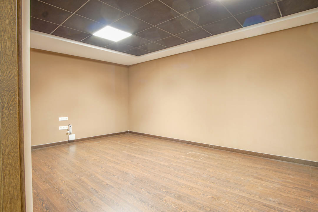 Multipurpose basement room featuring wood-effect flooring, neutral beige walls, and a suspended dark tile ceiling with integrated LED lighting.