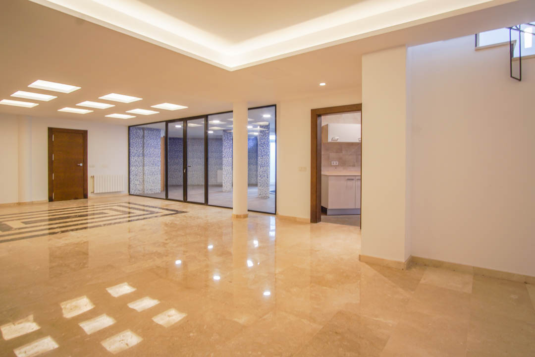 Spacious basement featuring polished marble floors, recessed LED lighting, and a glass-enclosed wellness area finished with blue mosaic tiling.