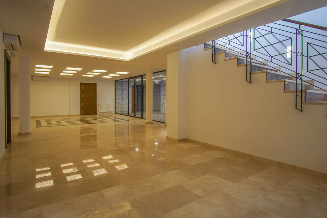 Spacious basement lounge featuring polished marble floors, integrated LED ceiling lighting, and glass partitions leading to the wellness area.