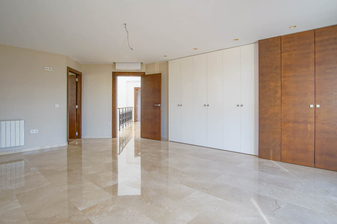 Spacious bedroom featuring polished marble floors, large dual-tone built-in wardrobes, and integrated air conditioning. The room offers natural light and high-quality wood finishes.