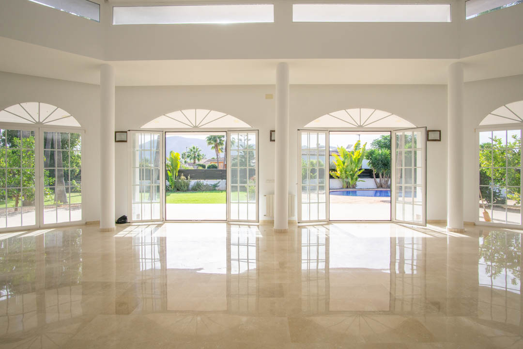 Spacious colonial-style living area featuring polished marble floors, white columns, and arched French doors opening onto the garden and private pool.
