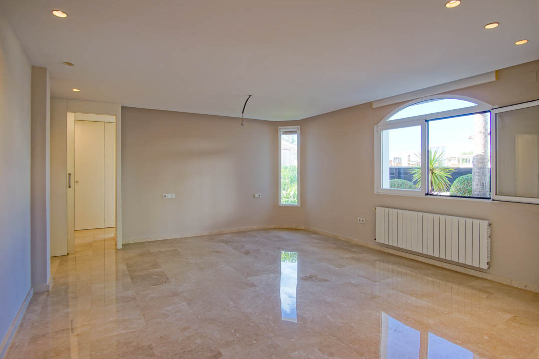 Spacious room featuring polished marble flooring, recessed spotlights, and an arched window providing natural light and views of the garden.