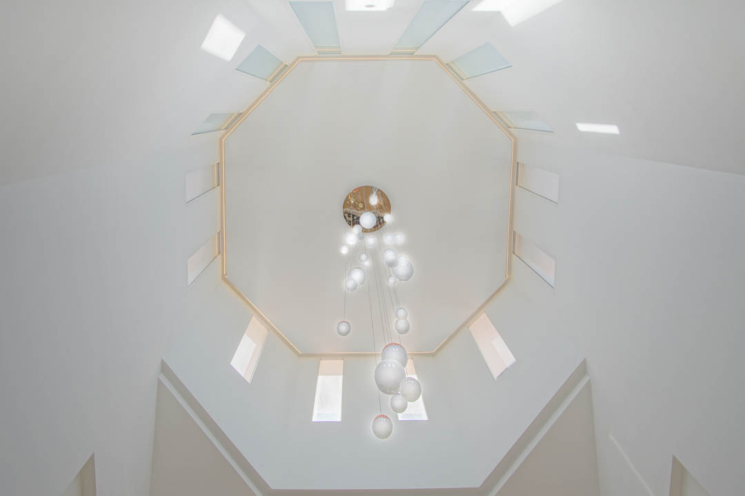Upward view of the octagonal ceiling featuring symmetrical skylights and a modern multi-sphere glass chandelier within the double-height stairwell.