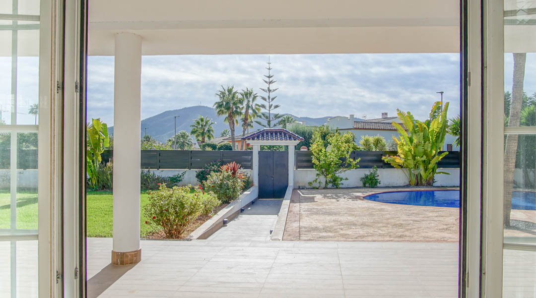 View from the interior looking onto the covered porch and garden, featuring a private pool and mountain views framed by white-trimmed glass doors.