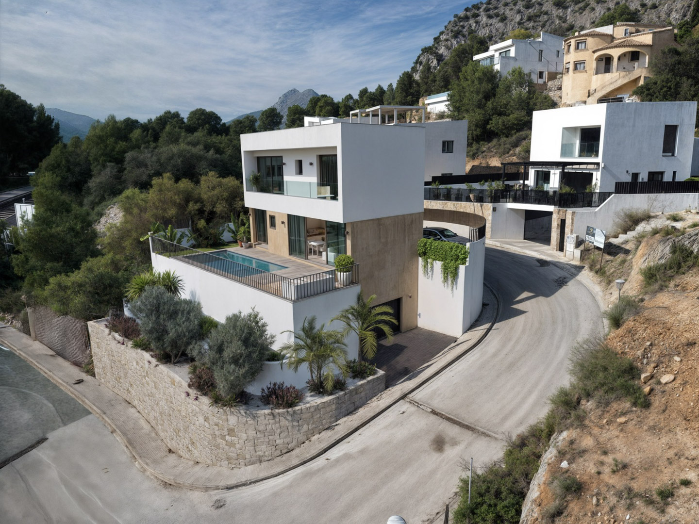 Exterior view of the modern villa featuring a white cubist design, stone-textured levels, a private pool terrace, and panoramic mountain backdrops.