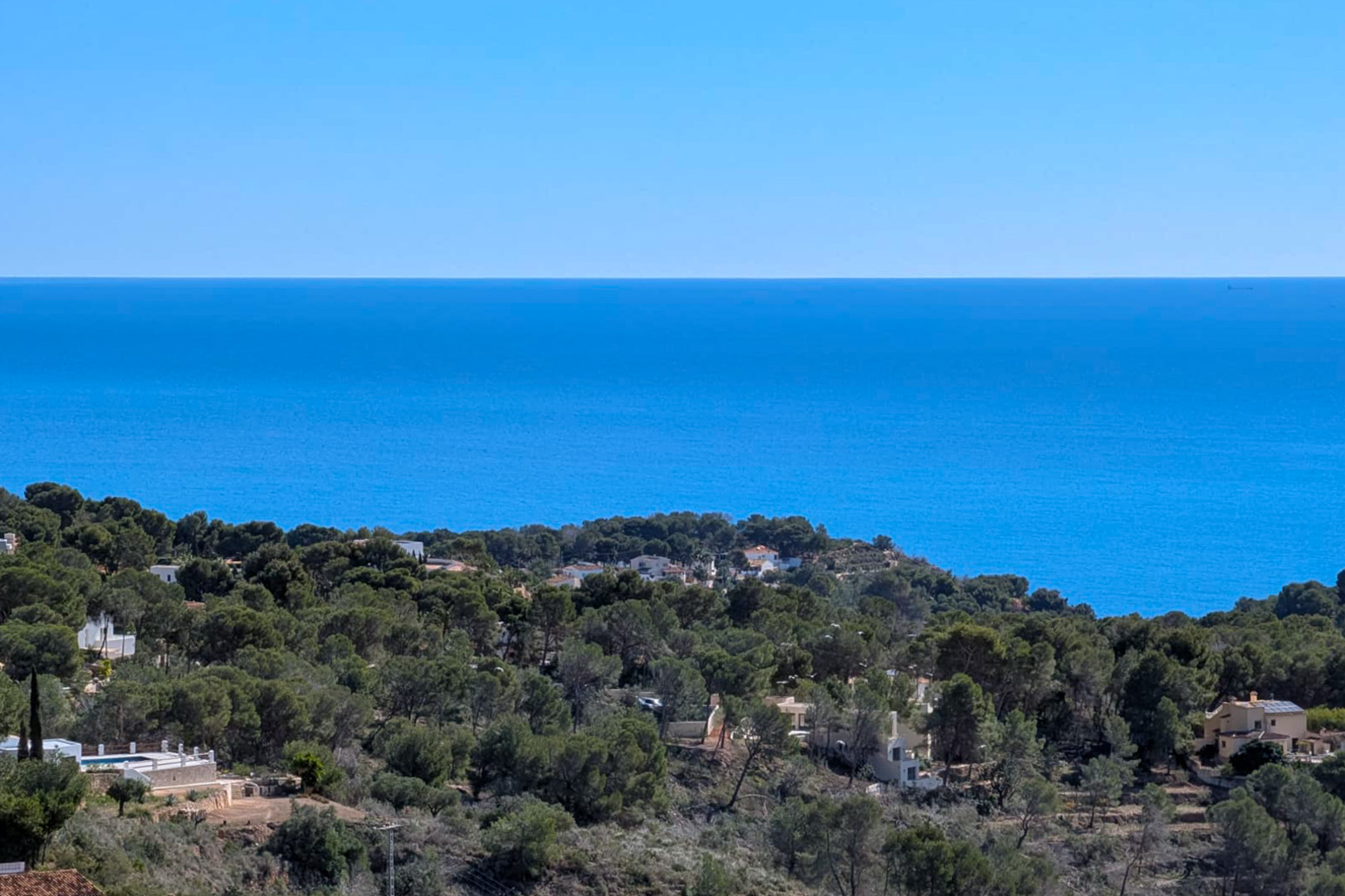 Elevated panoramic view from the plot overlooking the Mediterranean Sea and the pine-covered hillsides of Benissa under a clear sky.
