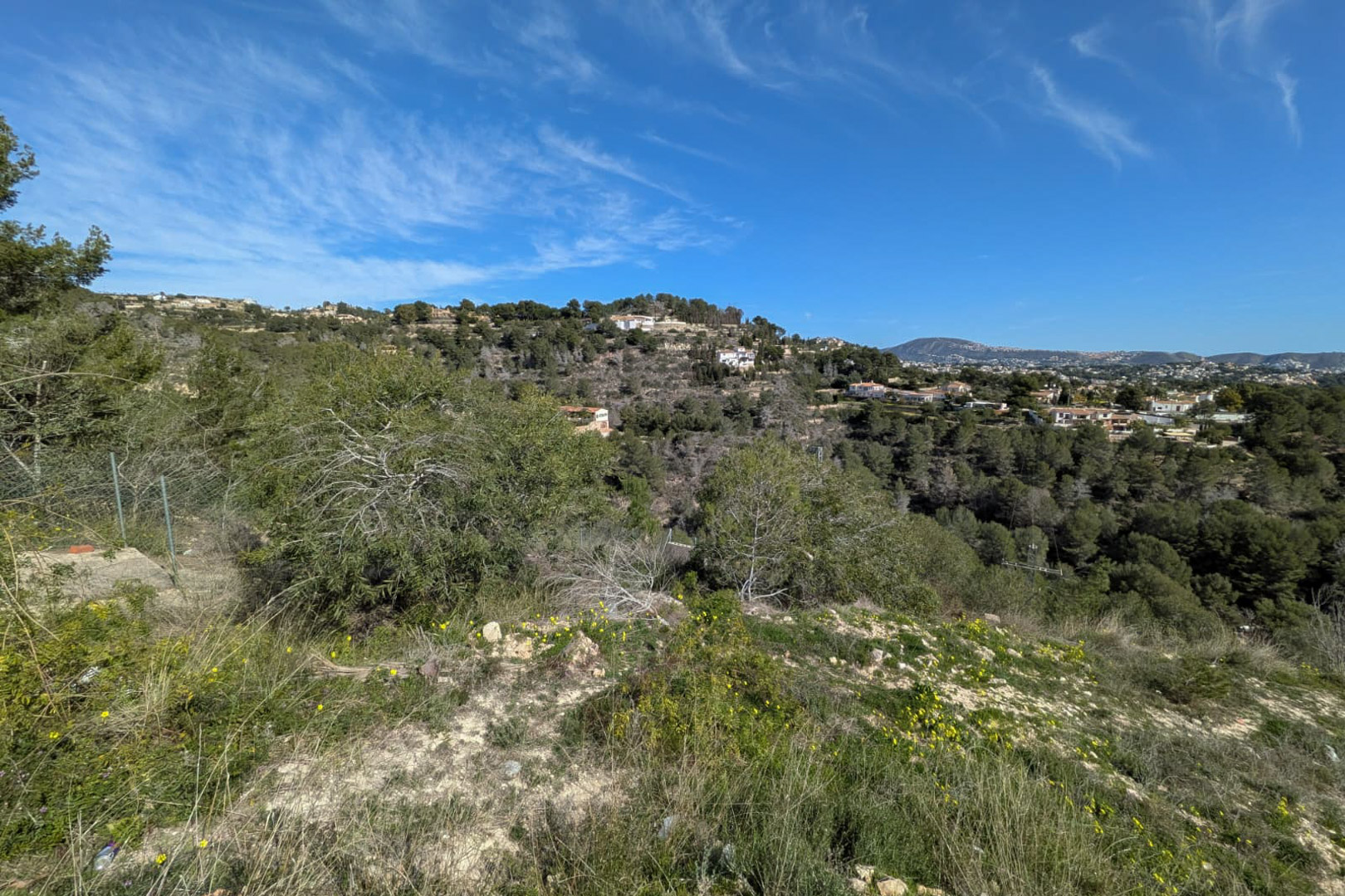 Elevated view from the steep plot showcasing native vegetation and the forested hills of Benissa under a clear blue sky.