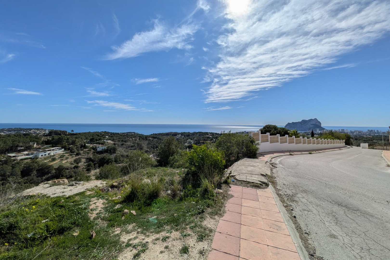 Panoramic view from the access road, showcasing the Benissa coastline, the Mediterranean Sea, and the Peñón de Ifach silhouette on the horizon.