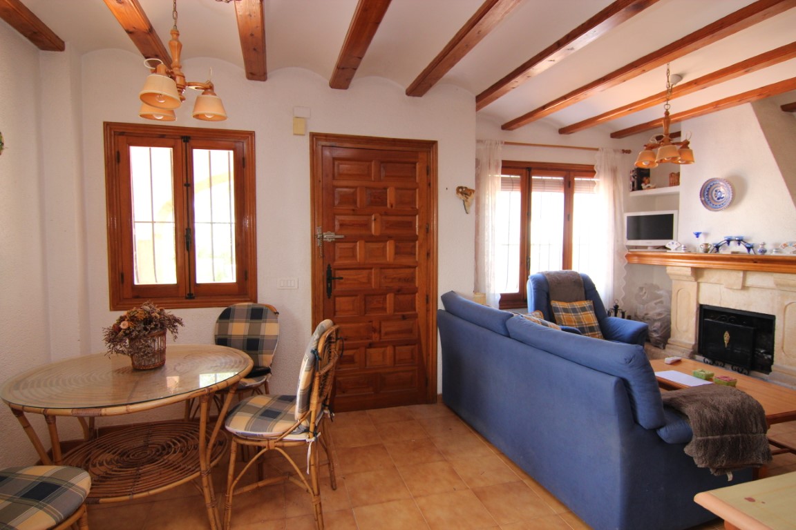 Rustic living and dining area featuring exposed wooden ceiling beams, terracotta floor tiles, a stone fireplace, and traditional wooden doors and window frames.