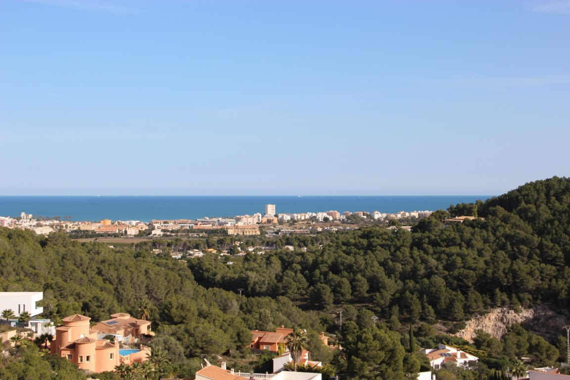 Panoramic views of the Mediterranean Sea and the Javea coastline from the elevated plots, surrounded by a dense pine forest landscape.