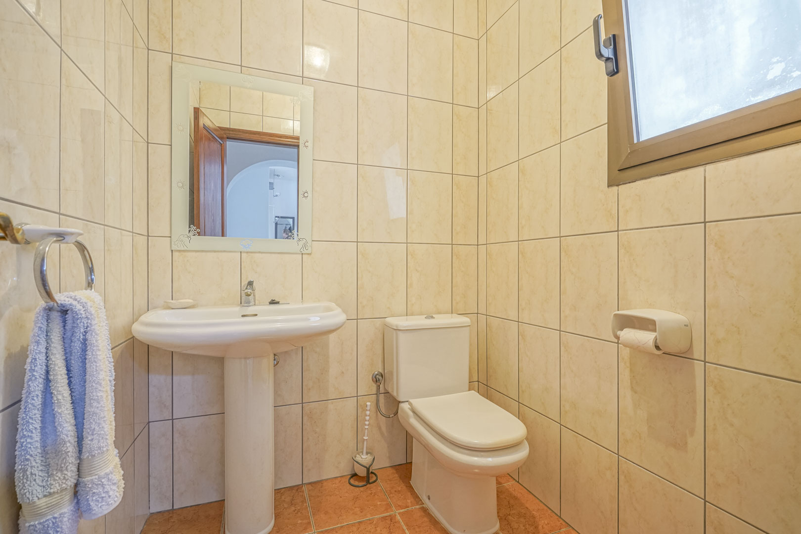 Bathroom featuring cream-colored tiles, a white pedestal sink, and a decorated mirror.