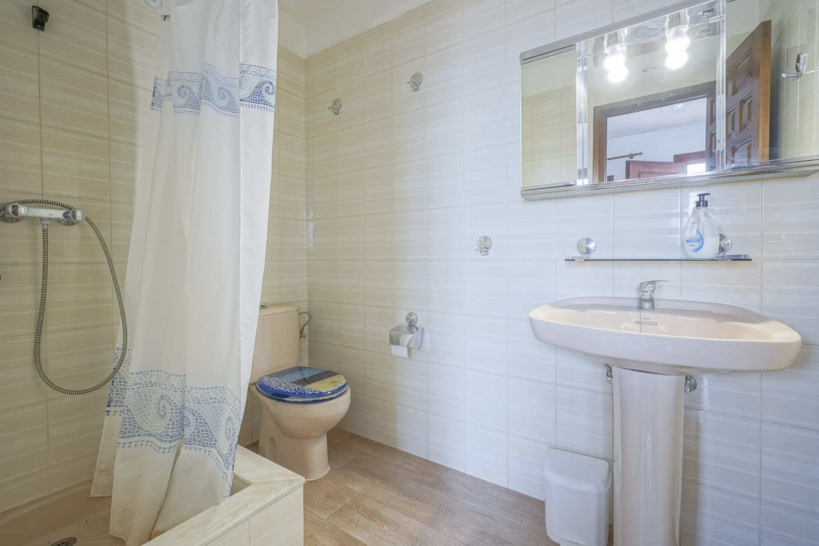 Bathroom featuring light tile, a pink pedestal sink, and a shower curtain with blue patterns.