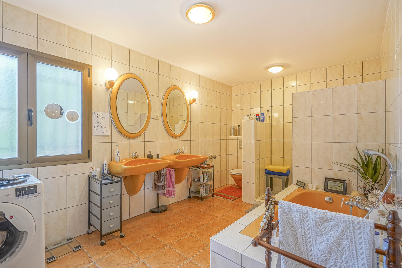 Bathroom featuring orange sinks and matching tub, cream-colored tiles, and a window with natural light.