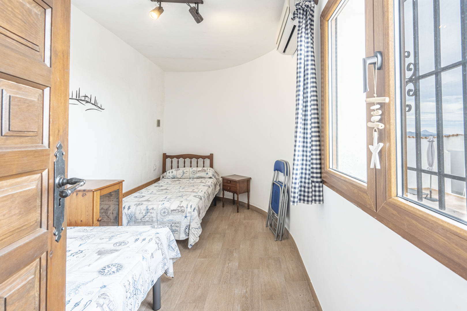 Bright bedroom featuring twin beds, nautical decor, and exterior views from the wood-framed window.