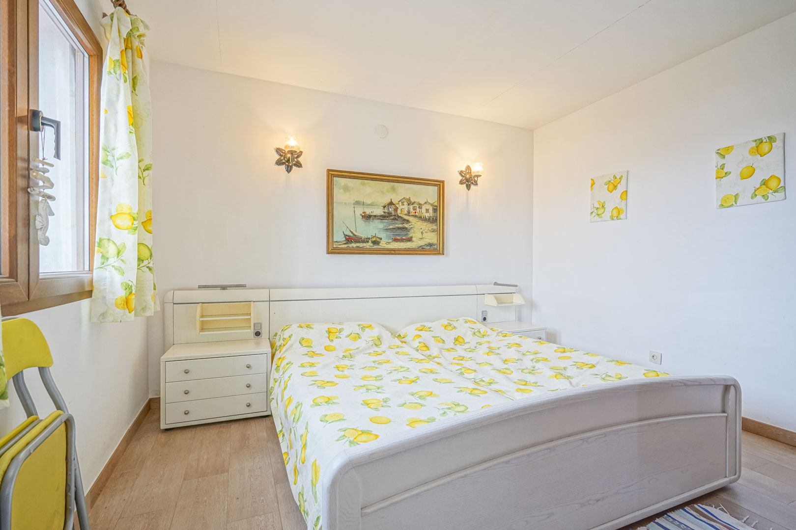 Bright bedroom with double bed, white headboard with built-in nightstands, and lemon-themed decor.