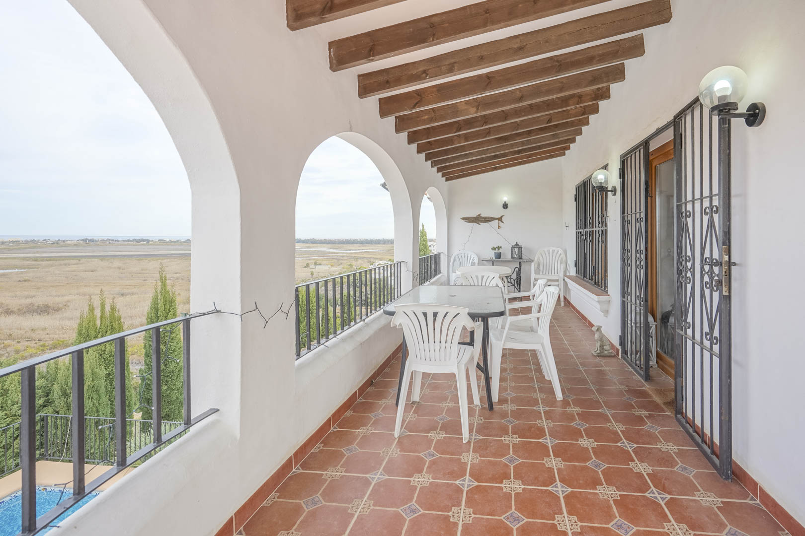 Covered terrace with panoramic views, white arches, and rustic tiled floor. Outdoor furniture.