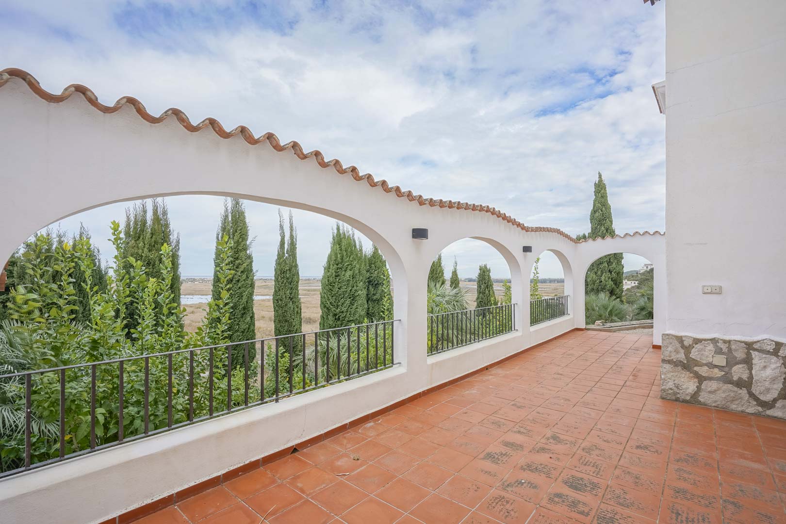 Covered terrace with tiled arches and rustic tile flooring, offering views of greenery and the landscape.