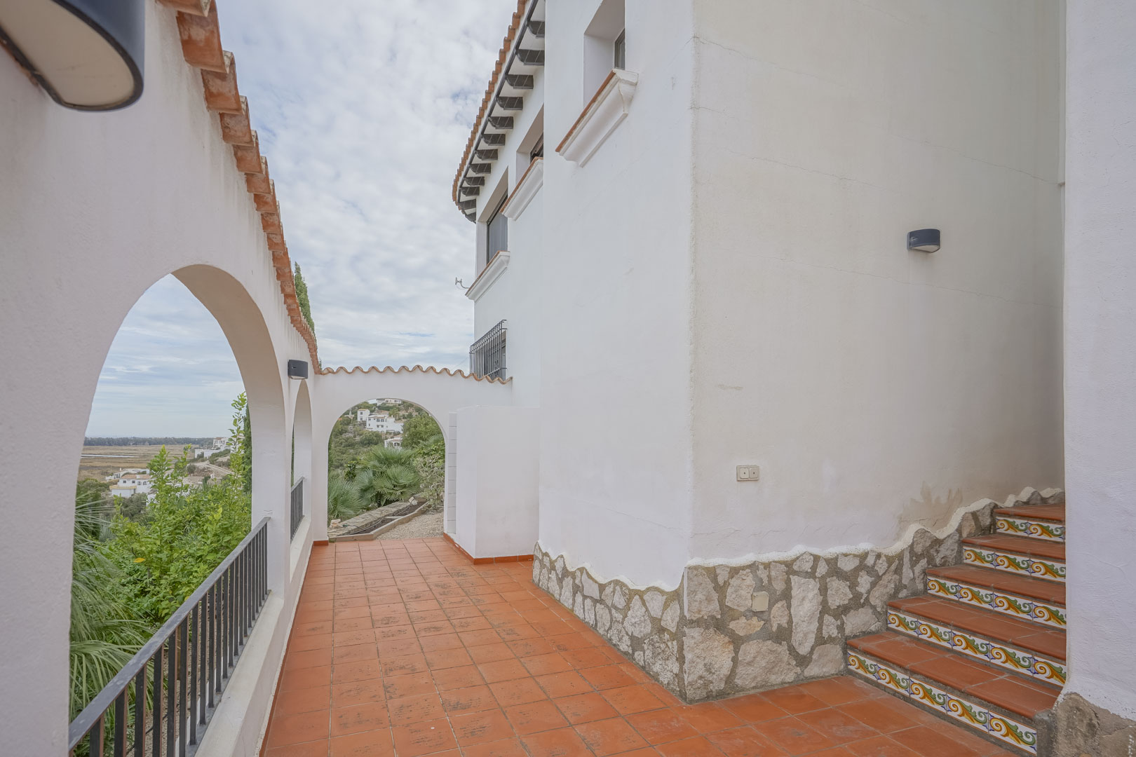 Exterior view of the villa featuring Spanish-style arches, terracotta terrace, and decorative stairs.
