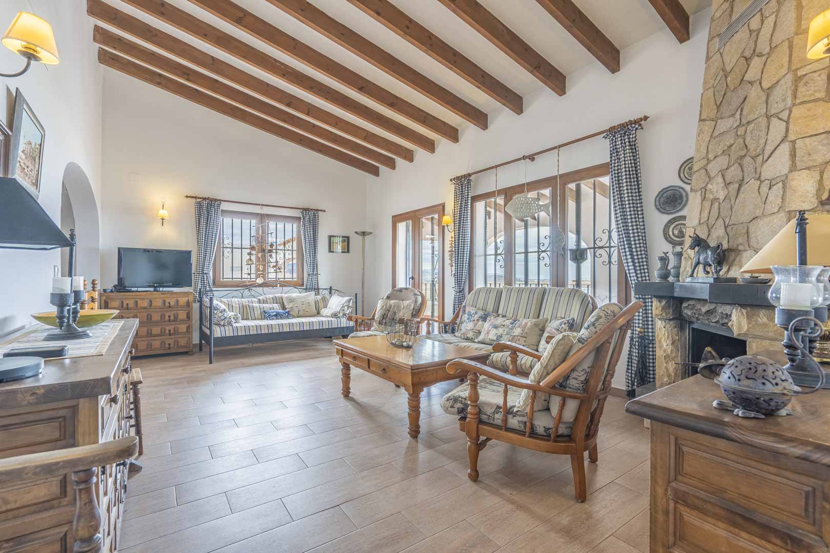 Living room featuring wood beams, a stone fireplace, and rustic furniture.