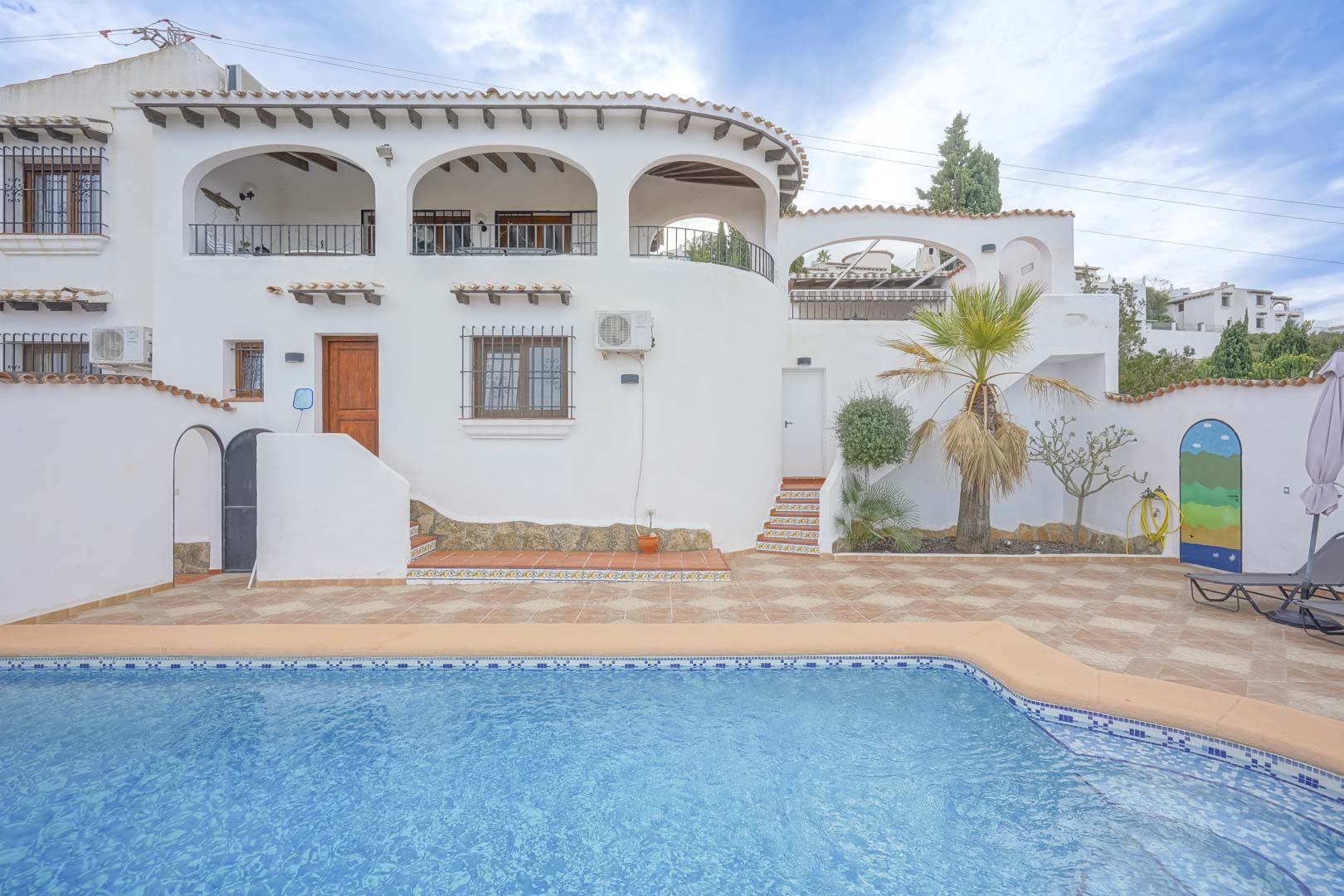 View of the villa's main facade featuring a pool, tiled terrace, and landscaping.