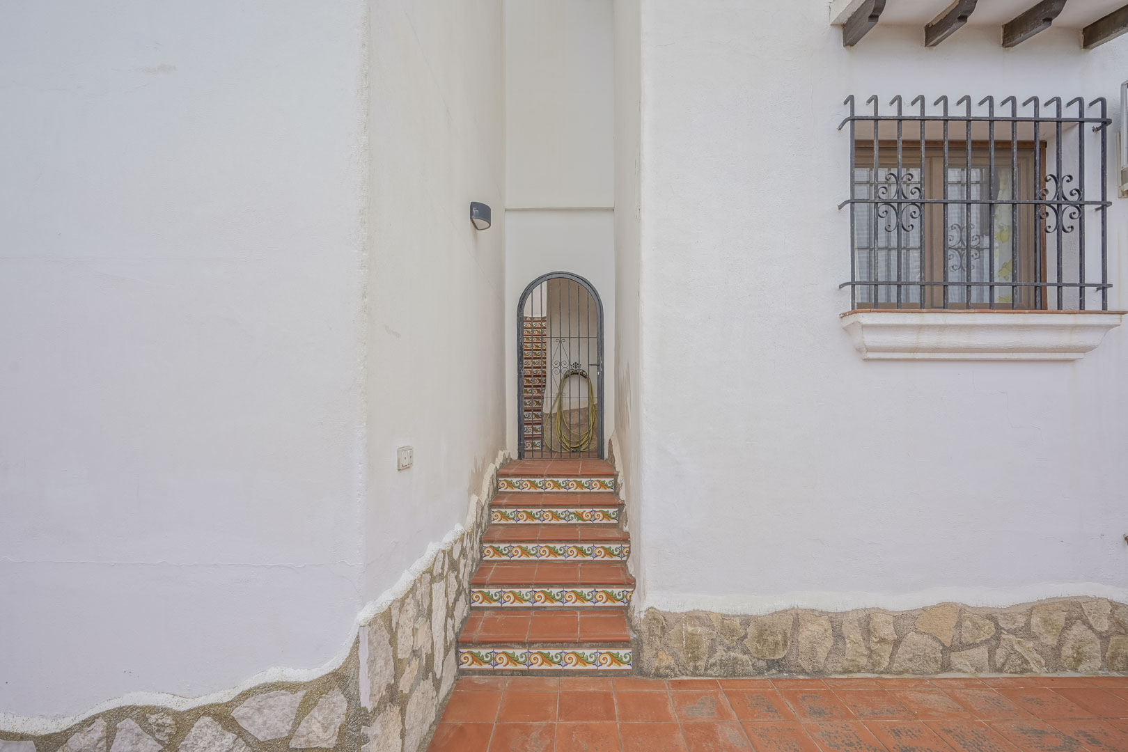 Villa entrance with decorated ceramic steps and wrought iron gate, rustic details on the white facade.