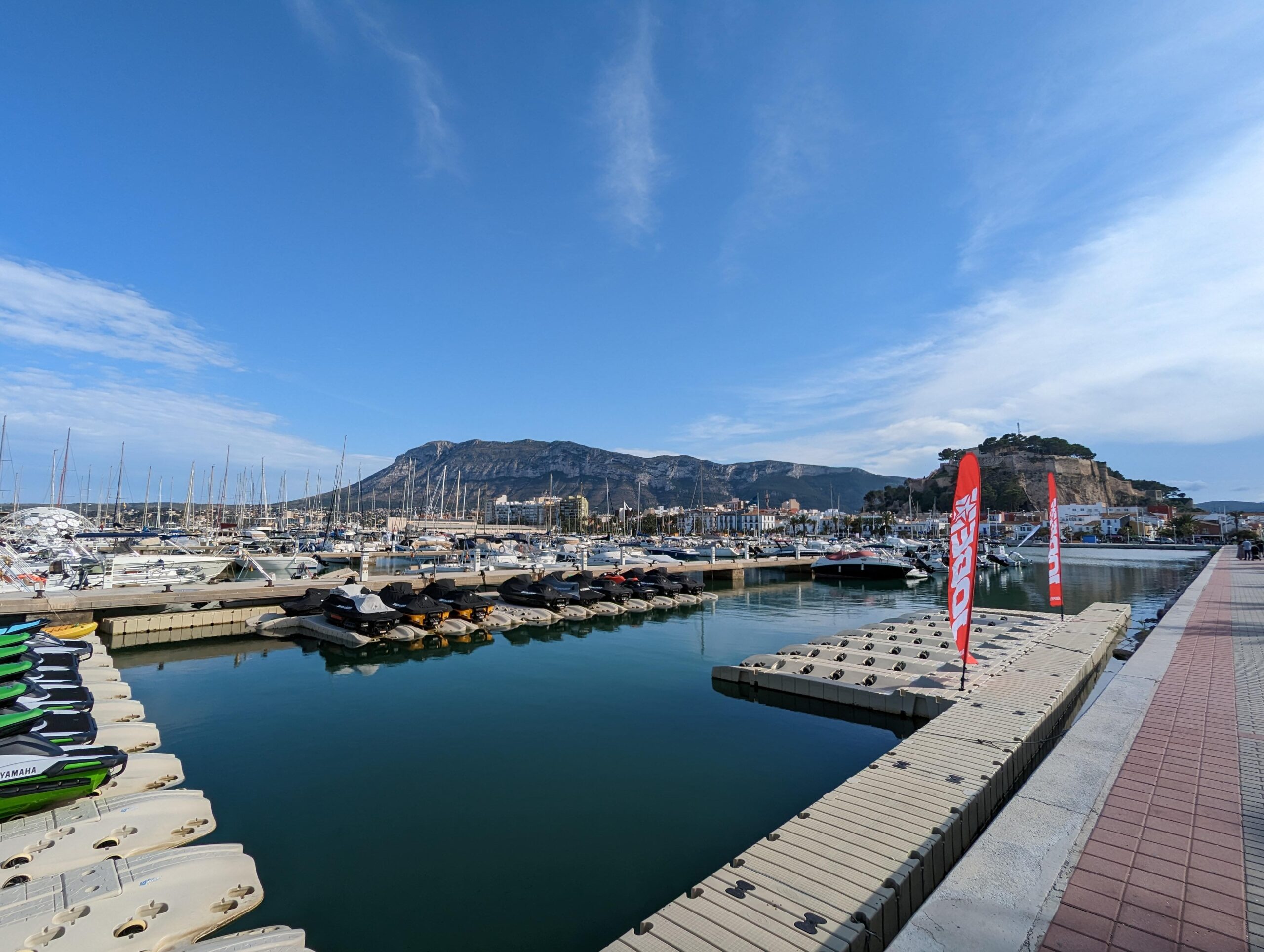 Marina view with jet skis and yachts, set against a mountain backdrop.