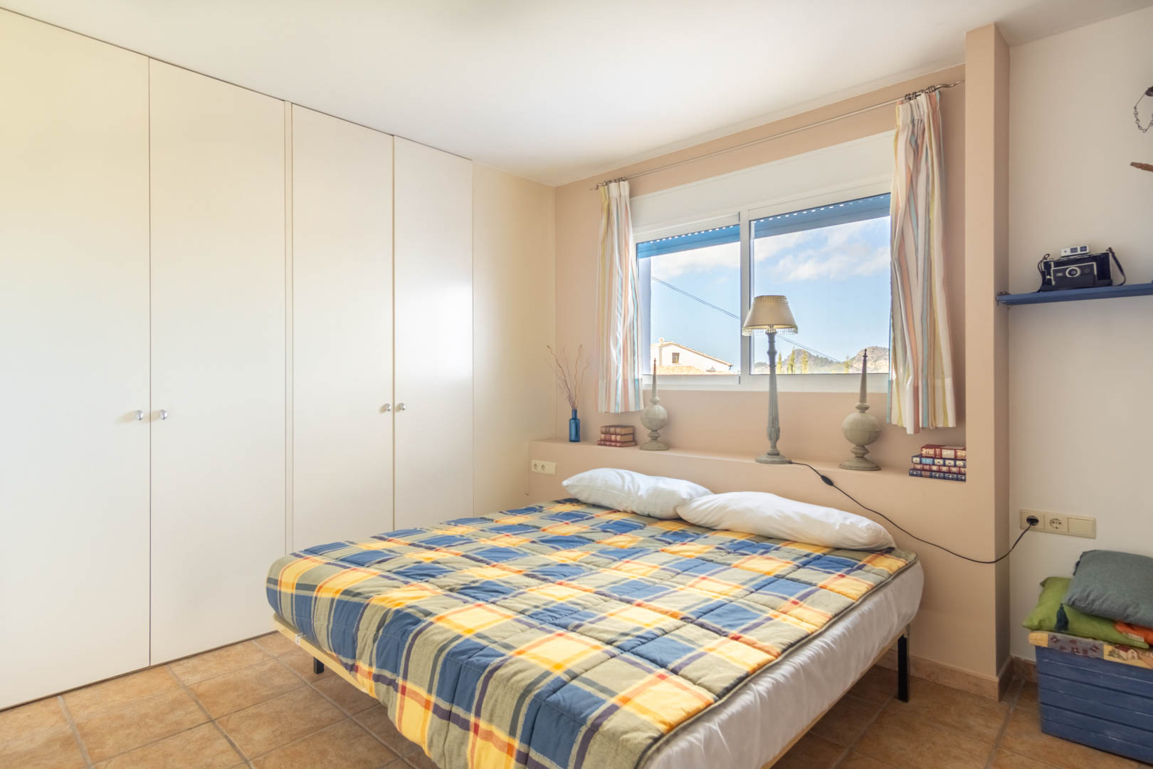 Bedroom featuring large white built-in wardrobes, rustic ceramic tile flooring, and a window with natural light overlooking the surrounding mountains.