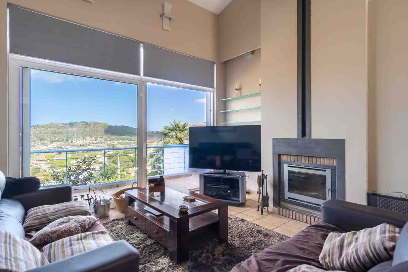 Bright living area featuring a built-in fireplace, terracotta flooring, and floor-to-ceiling windows overlooking the scenic valley and mountains.