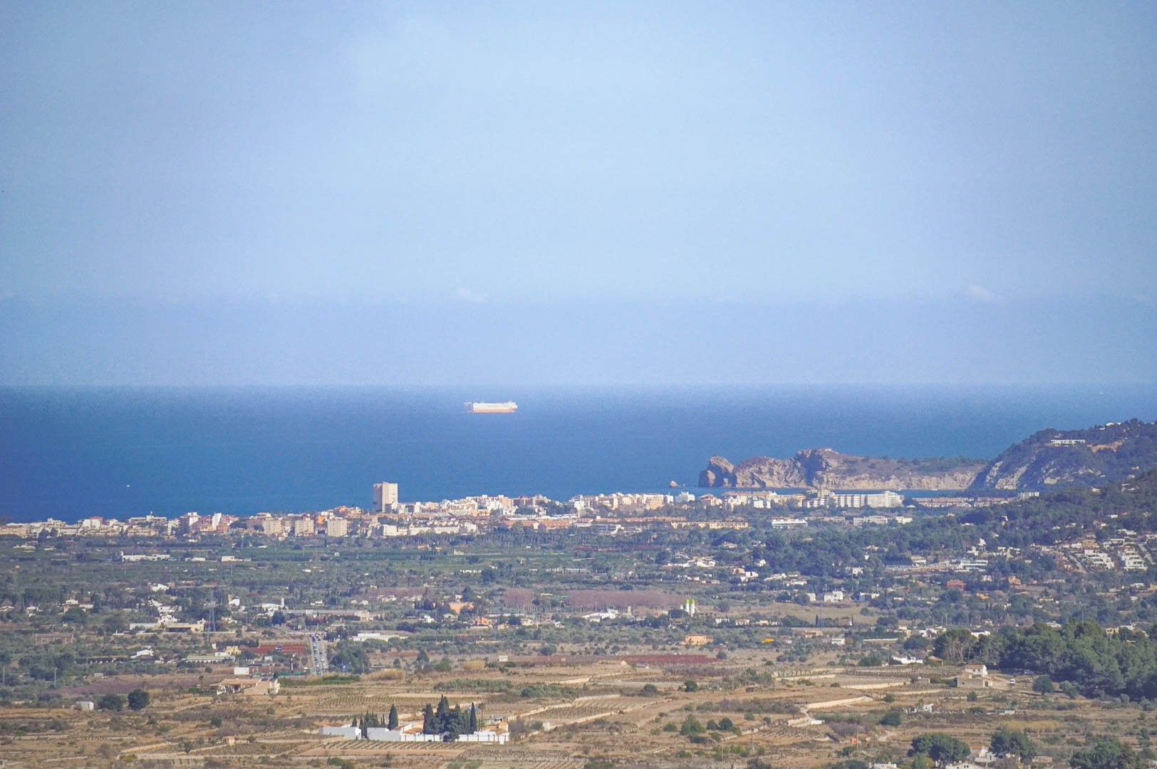 Clear panoramic views towards the Mediterranean coast, featuring the coastal town skyline and the sea with ships visible on the horizon.
