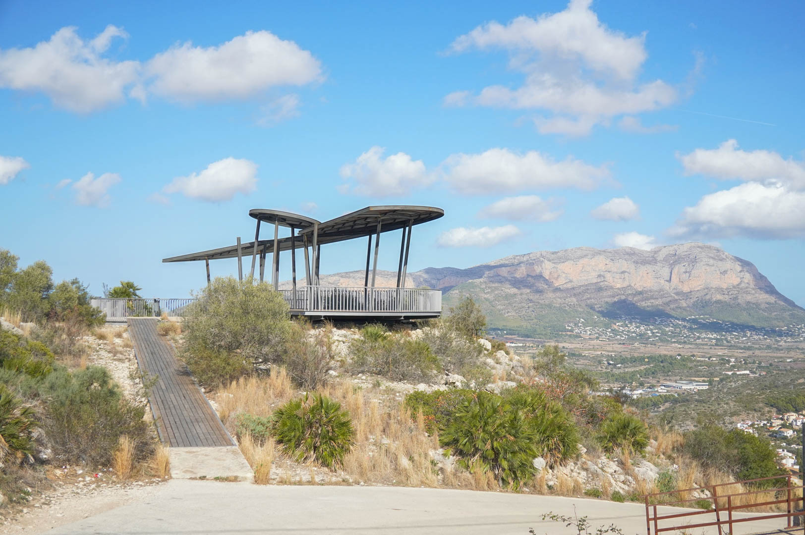 Contemporary viewpoint featuring a metallic structure and wooden walkway, providing panoramic views of the valley and the Montgó mountain range.