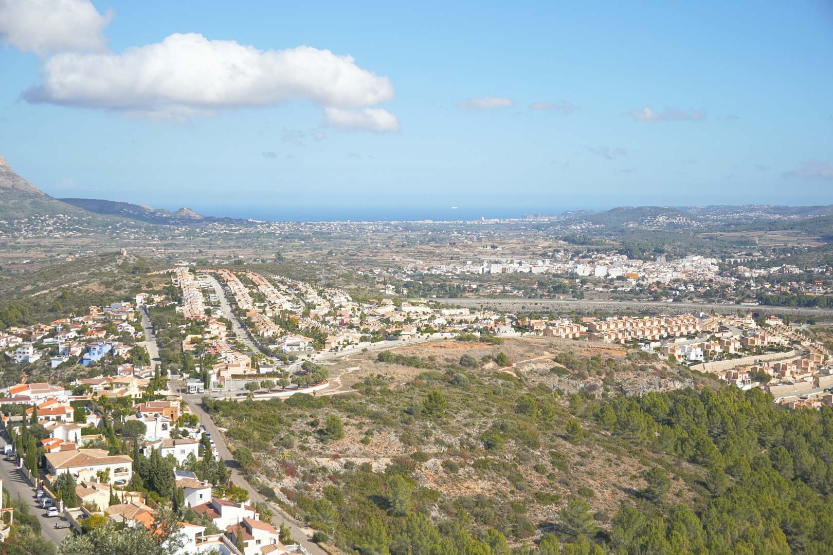 Elevated panoramic views overlooking the Pedreguer valley, residential areas, and the Mediterranean Sea horizon under a clear blue sky.