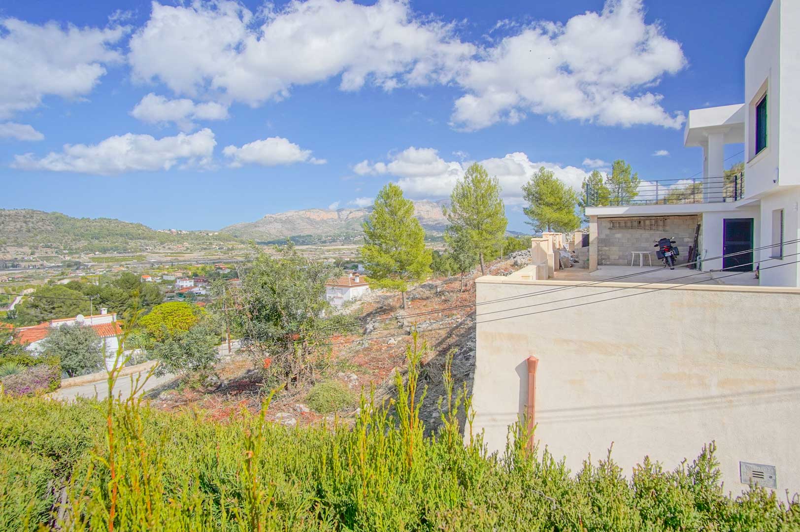 Exterior view of the villa's terrace and parking area, highlighting the expansive panoramic views of the valley and distant mountain ranges.