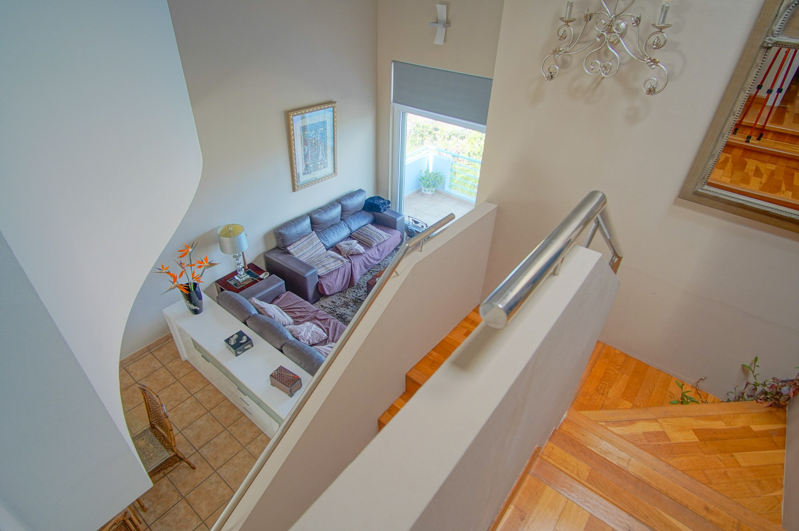 High-angle view of the wooden staircase with stainless steel railings, overlooking a double-height living room with access to an outdoor terrace.