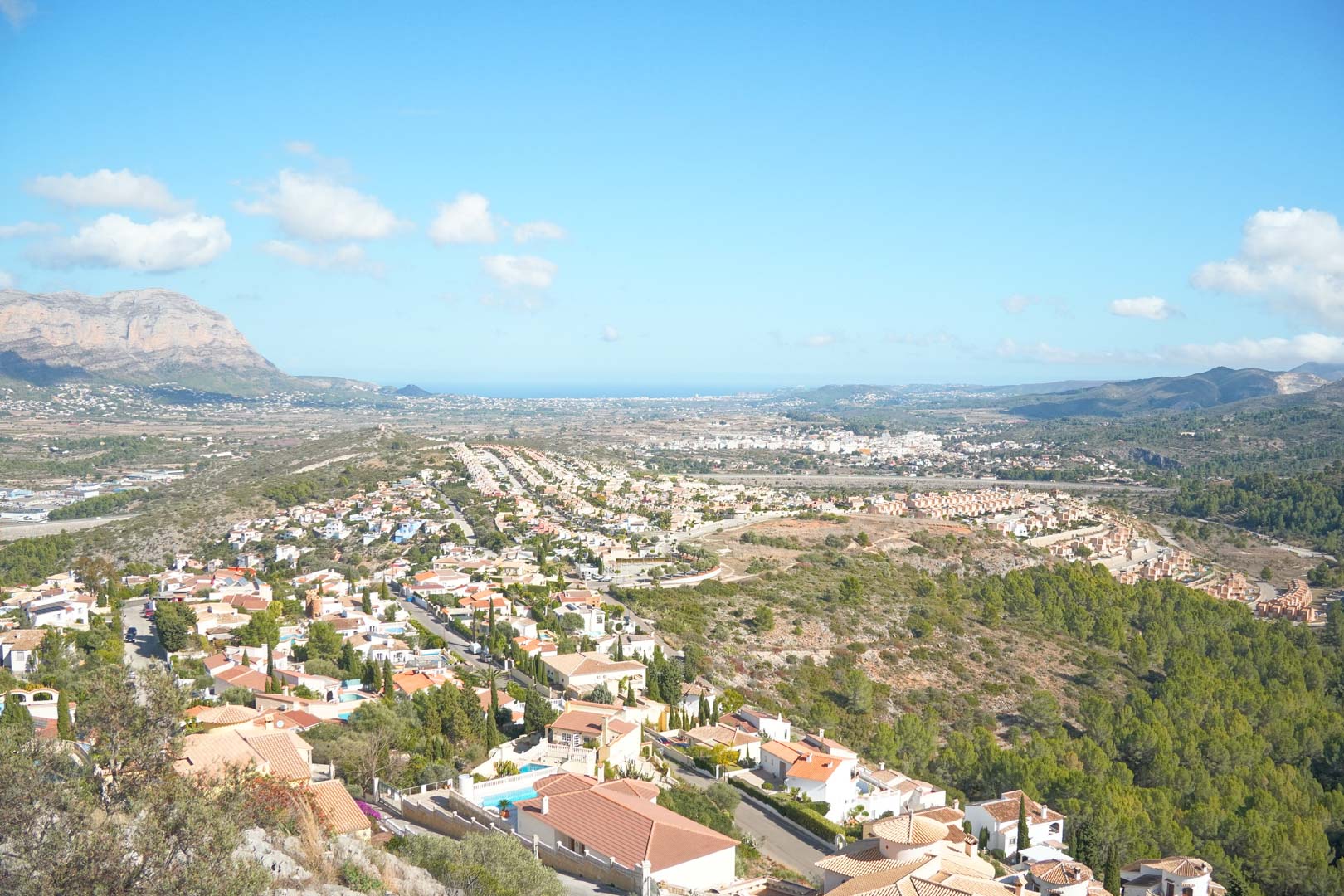 Panoramic elevated views overlooking the Pedreguer valley towards the Mediterranean Sea, featuring residential areas nestled among pine forests and mountains.