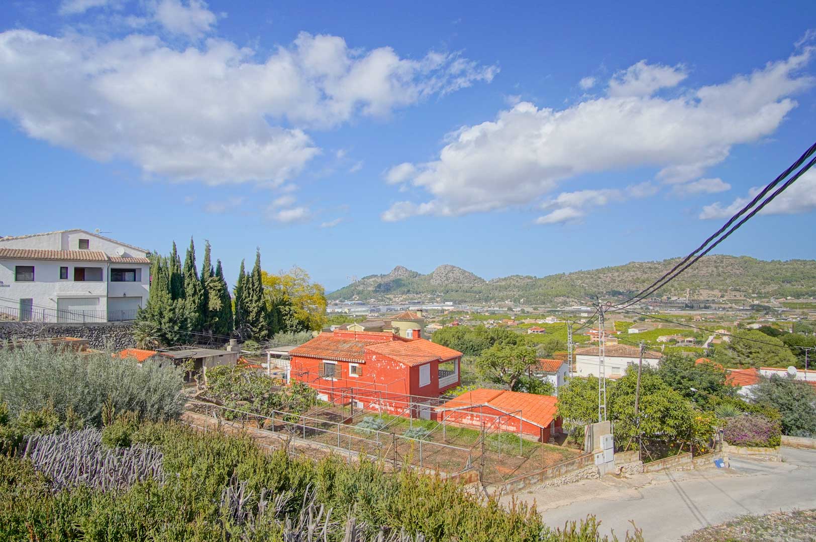 Panoramic view from the property overlooking the Pedreguer valley and mountains, featuring Mediterranean vegetation and a quiet residential setting under a clear sky.