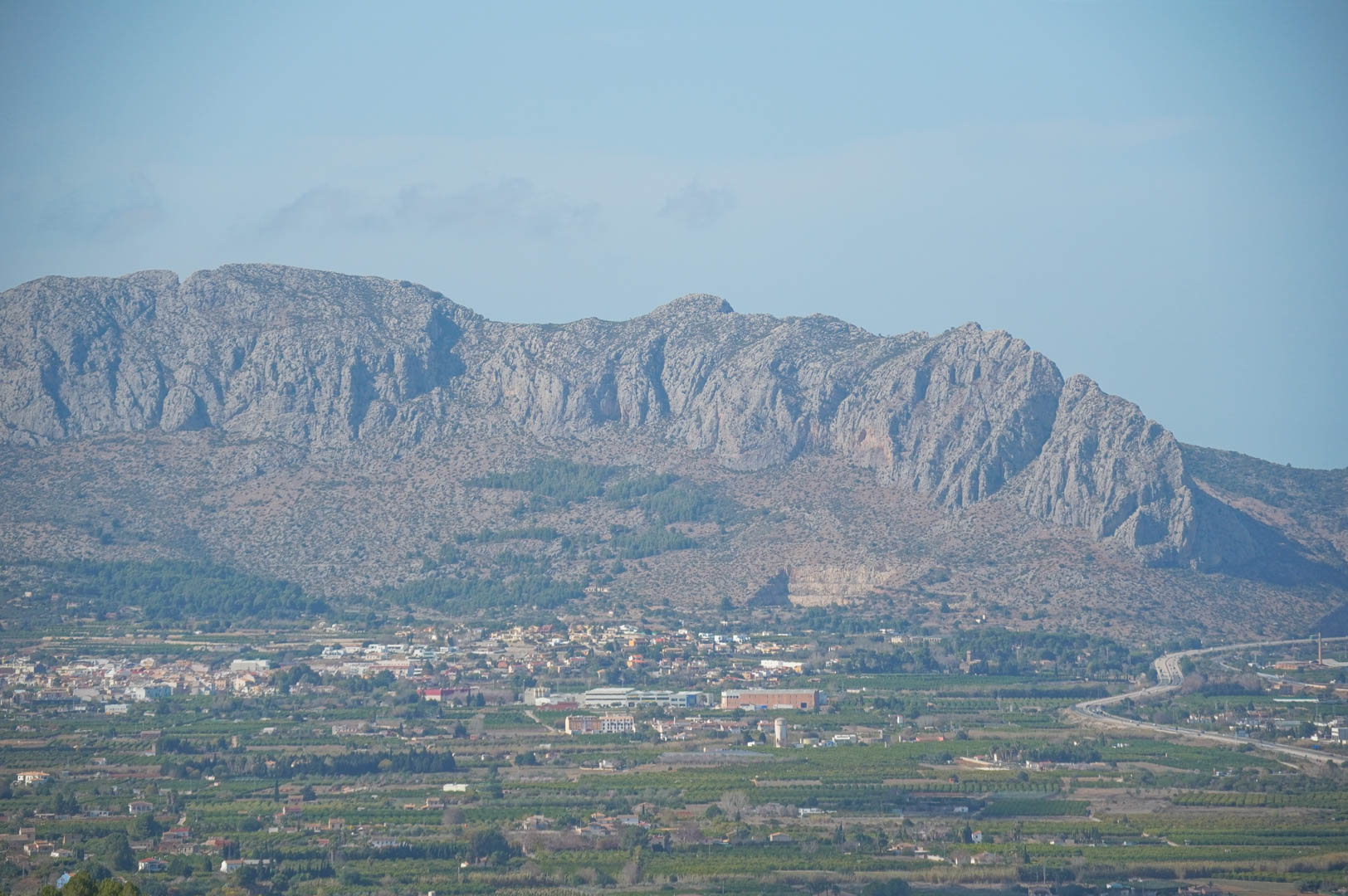 Panoramic views of the rugged mountain range and the lush valley, highlighting the strategic location near the highway and local Mediterranean landscape.