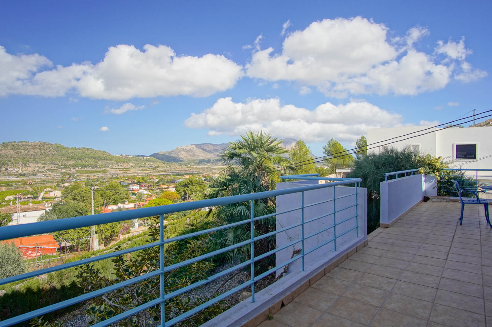 Upper terrace featuring tiled flooring and blue railings, overlooking the Pedreguer valley with expansive views of the Mediterranean mountains.