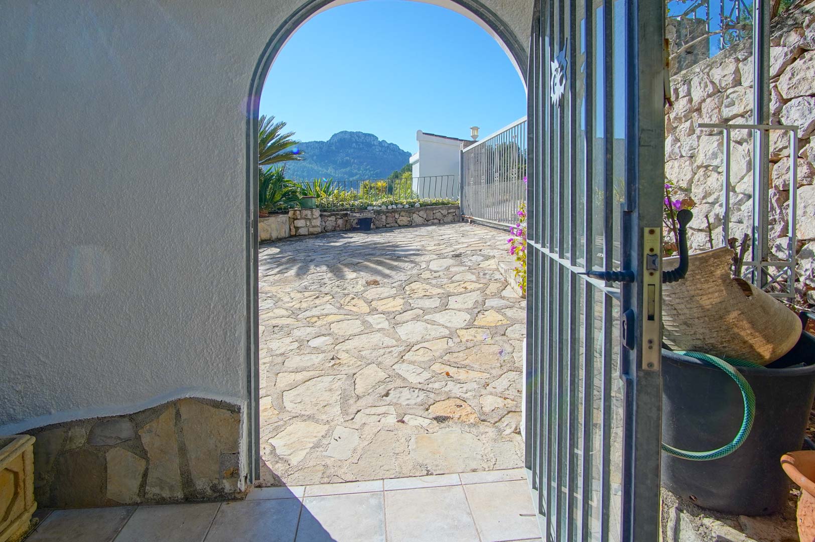 Arched doorway leading to an irregular stone patio with panoramic mountain views, featuring traditional stone walls and a metal security gate.