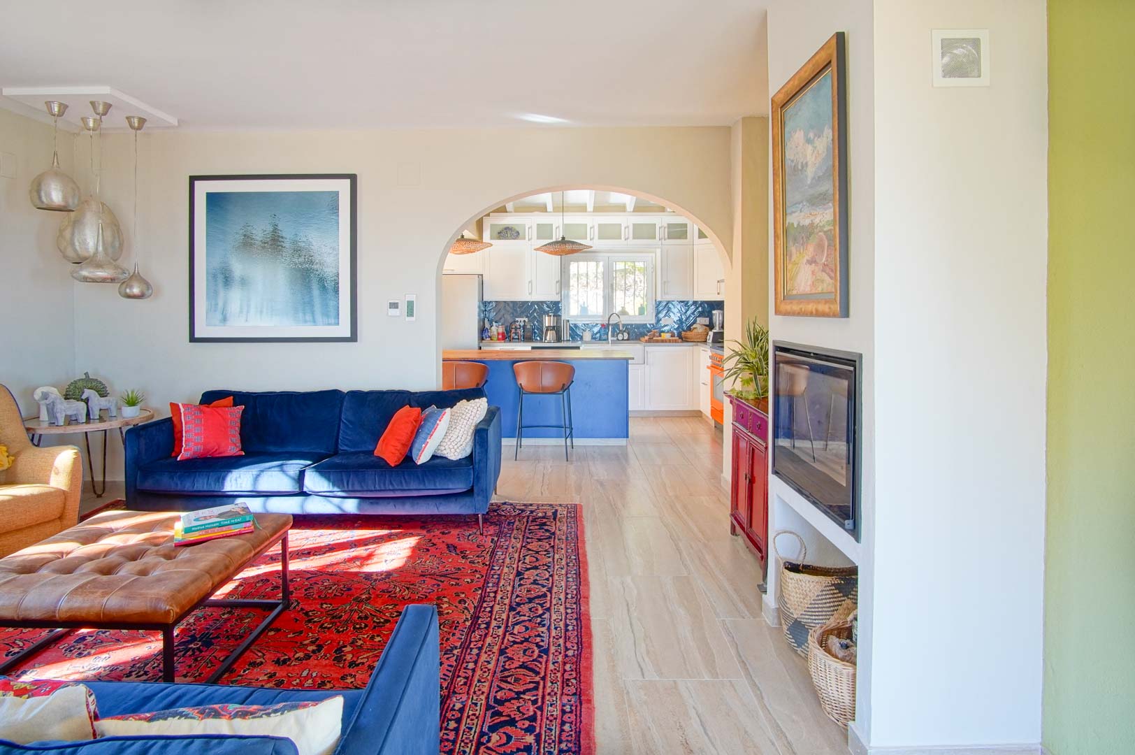 Bright living area featuring blue velvet sofas and a built-in fireplace, opening through an archway into a kitchen with a blue island and white cabinetry.